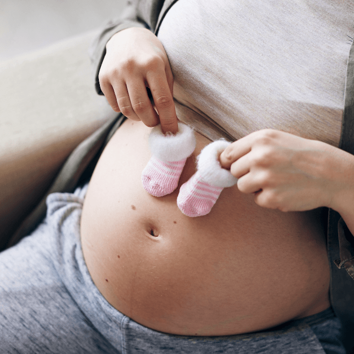 Young Pregnant Female Holding Tiny Socks Over Her Belly